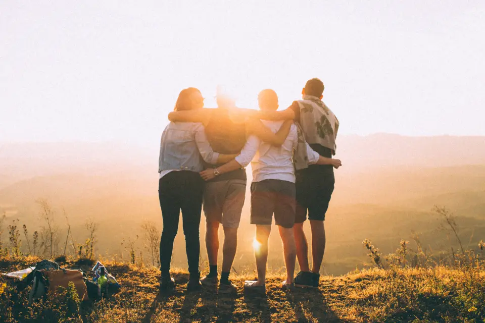 Friends arm in arm, watching the sun set over the mountains